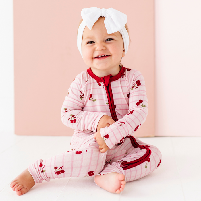 Baby wearing a pink and red outfit with cherry patterns on a light pink background