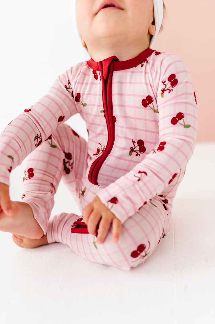 Baby wearing a pink outfit with red accents and cherry patterns on a white background