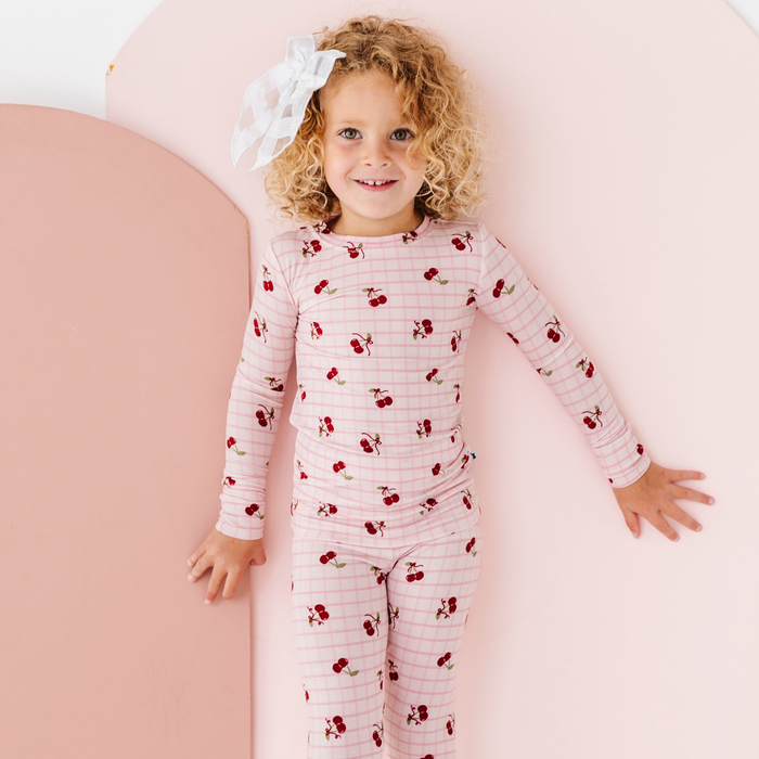 Child wearing a pink and red striped pajama set with cherry pattern on a pink background