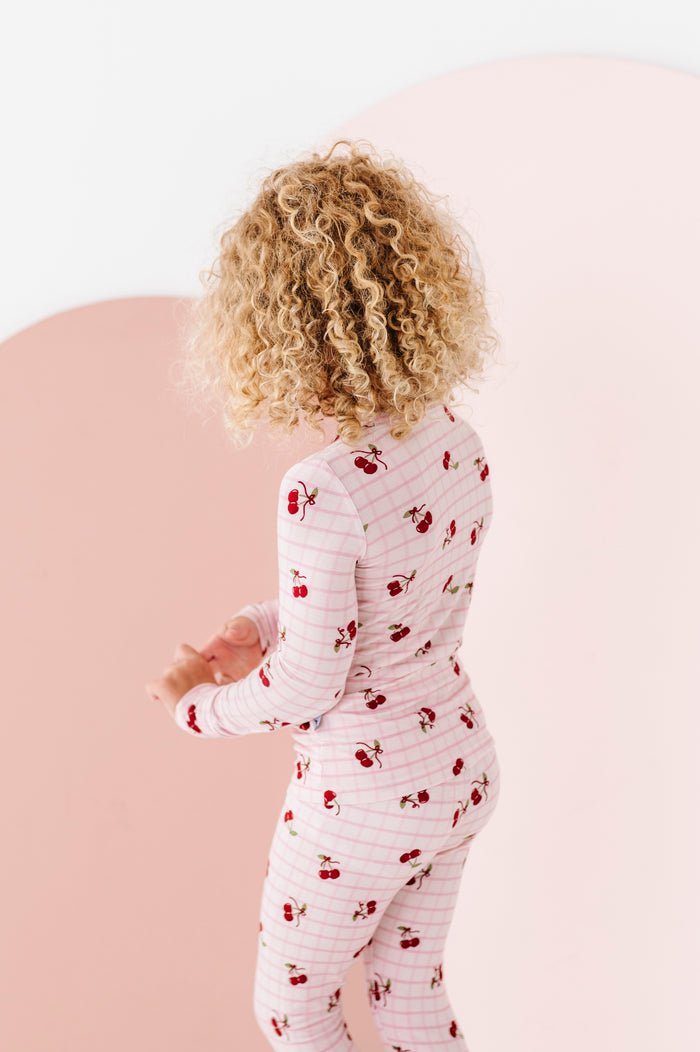 Child wearing a white onesie with red cherry pattern on a pink background