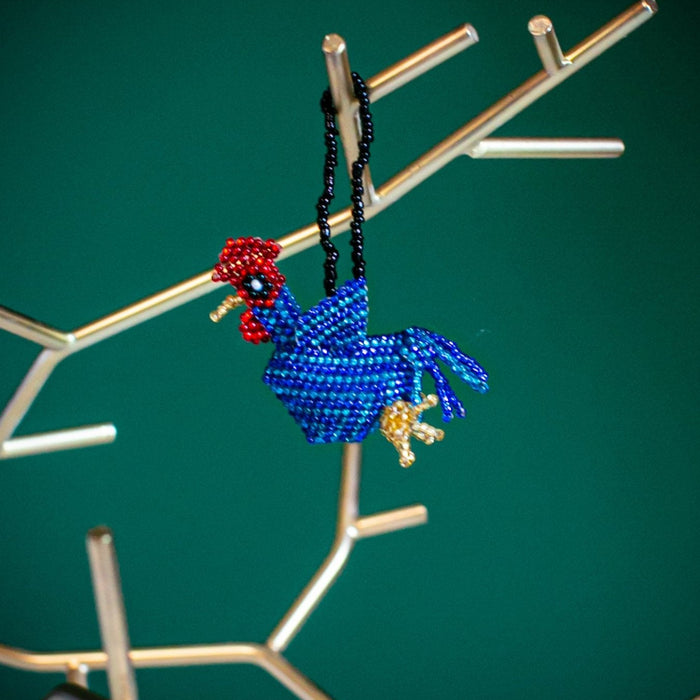 Blue beaded rooster ornament on a branch against a green background